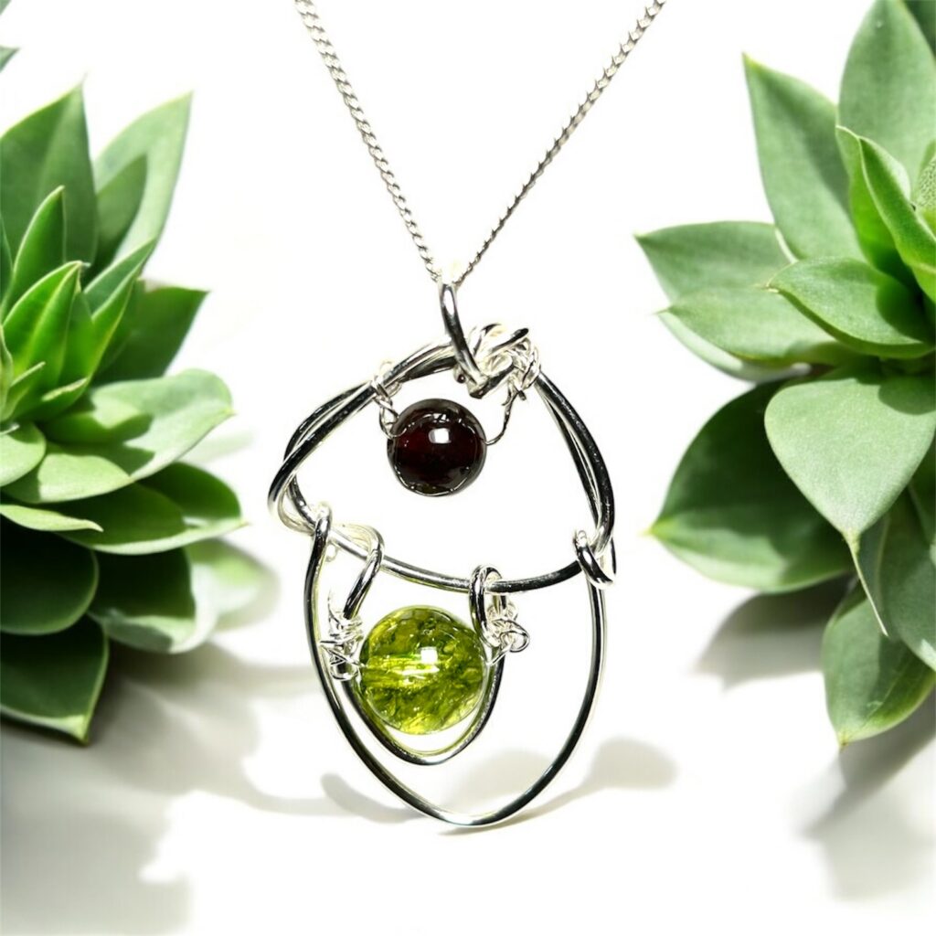 Contemporary garnet and peridot pendant handcrafted in sterling silver. A modern gemstone necklace with rich red and vibrant green stones, perfect for gifting.